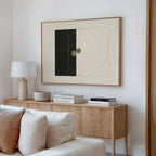 A modern living room features a light wood sideboard with books, a lamp, and a bowl. Above it hangs the Circular Tension Canvas Art with abstract geometric shapes. A white sofa sits in the foreground against a neutral wall.