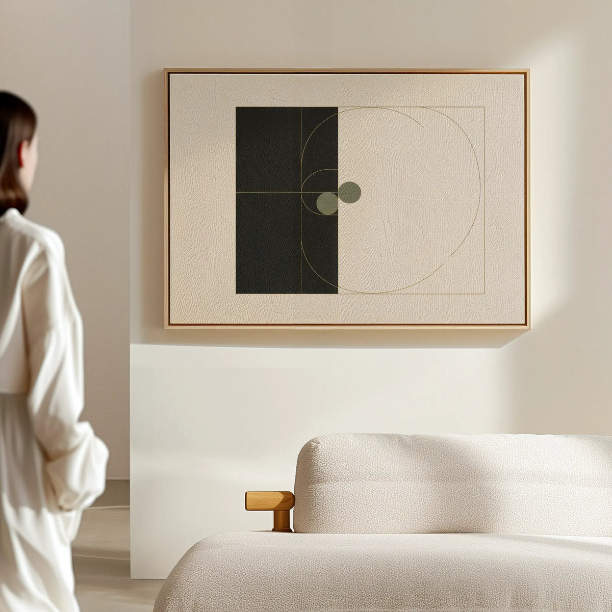 A person in a white outfit admires the Circular Tension Canvas Art—geometric wall decor in a wooden frame—hanging above a textured neutral sofa or bed in a minimalist modern living room.