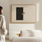 A person in a white outfit admires the Circular Tension Canvas Art—geometric wall decor in a wooden frame—hanging above a textured neutral sofa or bed in a minimalist modern living room.