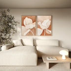 A modern living room with a cream sectional, wooden coffee table with lamp and book, leafy potted plant, and Clay Blossom Set of 2 floral wall art prints displayed on the wall.