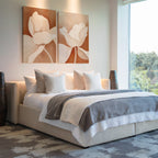 Modern bedroom with a large bed, white and gray bedding, and multiple pillows. Above the bed, the Clay Blossom Set of 2 floral wall art adds elegance. A large window lets in natural light, with tall vases on each side of the bed.
