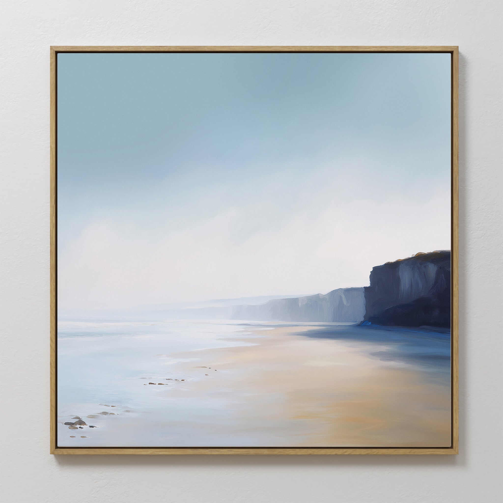Cliffside Light Canvas Art is a framed minimalist piece featuring a serene beach scene with a soft blue sky, gentle waves, sandy shore, and distant cliffs—perfect for adding tranquility to any white wall.