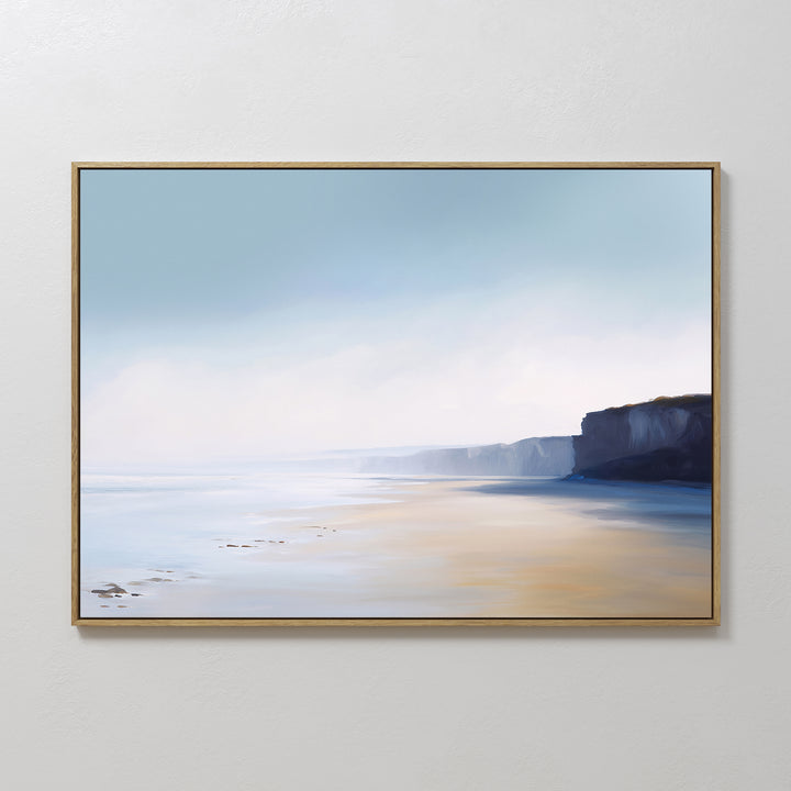 Cliffside Light Canvas Art – Horizontal features a serene coastal scene with a soft blue sky, misty horizon, calm water, sandy beach, and distant cliffs—perfect minimalist wall art for bedroom decor on a plain white wall.