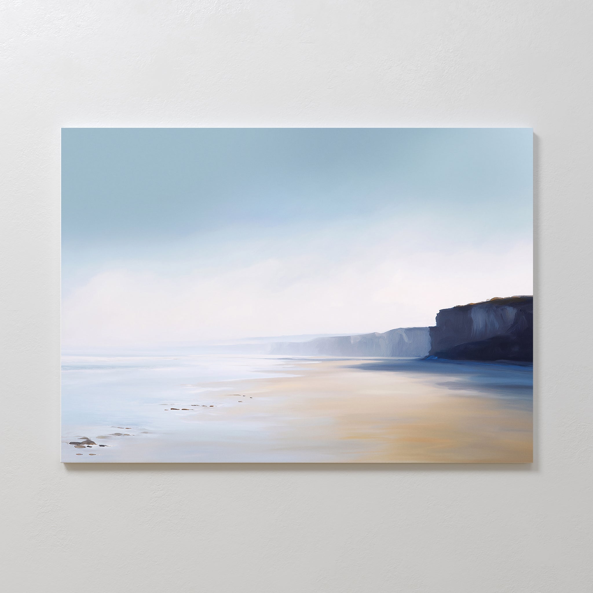Cliffside Light Canvas Art – Horizontal features a serene coastal scene with soft blue sky, mist, sandy beach, and distant cliffs. Its light tones create a calming mood, perfect as minimalist wall art or relaxing bedroom decor.