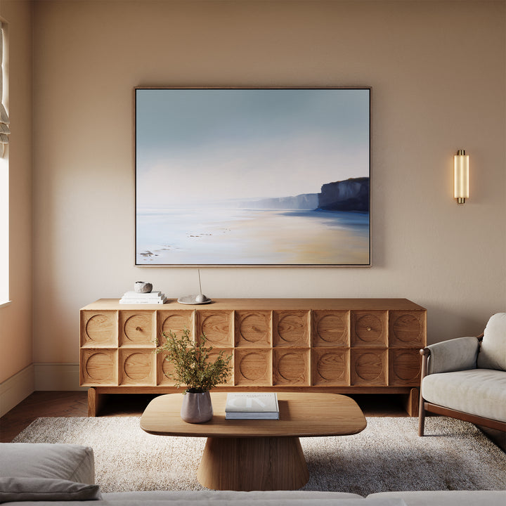 A modern living room with a light wood coffee table, textured-door sideboard, neutral rug, cream sofa, and the Cliffside Light Canvas Art – Horizontal displayed above the sideboard.