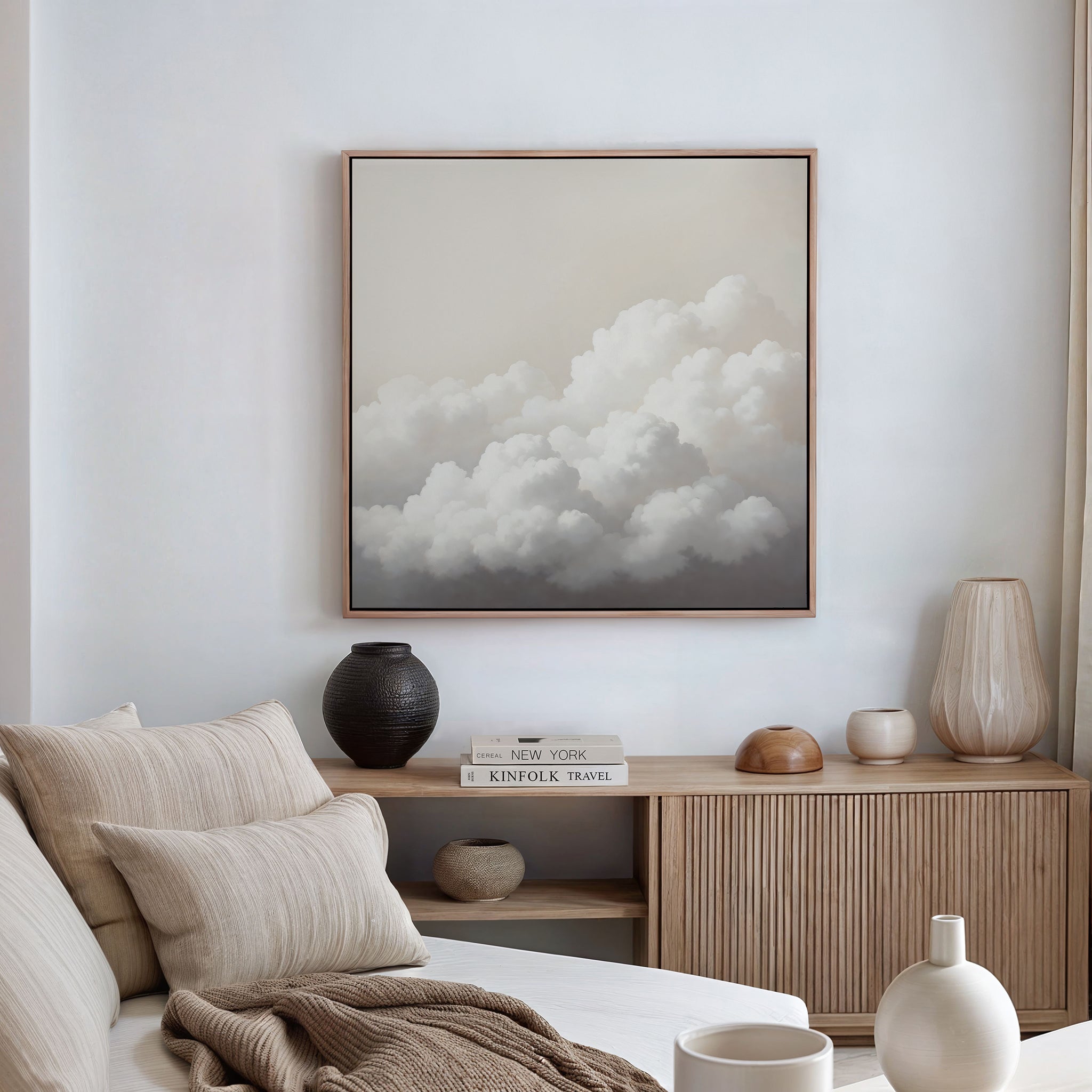 A minimal, neutral-toned living room with a beige sofa, wooden sideboard, ceramic vases, stacked books, and minimalist wall art. Soft natural light flows through cream curtains, accenting the Cloud Reverie Canvas Art on the wall.