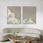 A minimalist living room with a curved beige sofa, a round wooden coffee table with white flowers, and the Clouded Dreams Set of 2 wall art prints—perfect for adding elegant style to your decor.