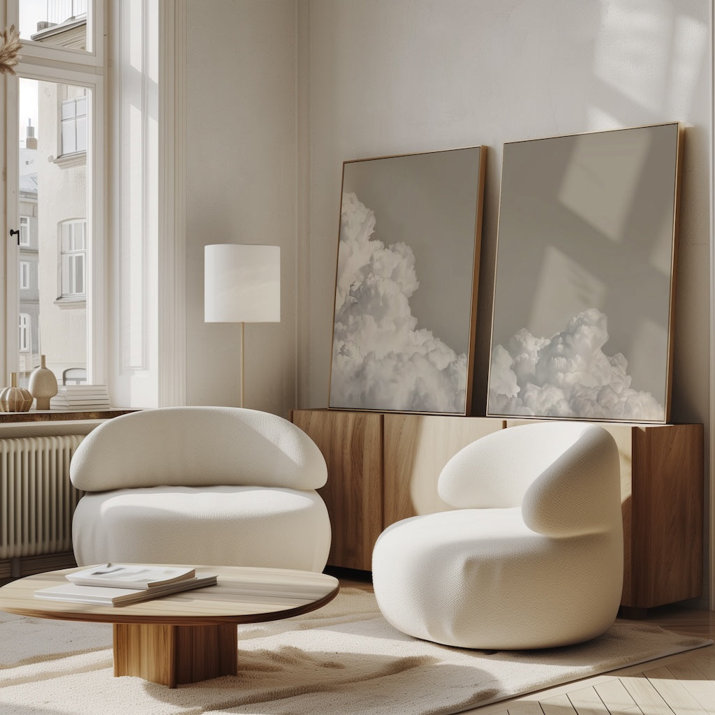 A modern living room featuring two rounded white lounge chairs, a low wooden coffee table, large windows, and the Clouded Dreams Set of 2 wall art prints—perfect inspiration for contemporary living room decor.