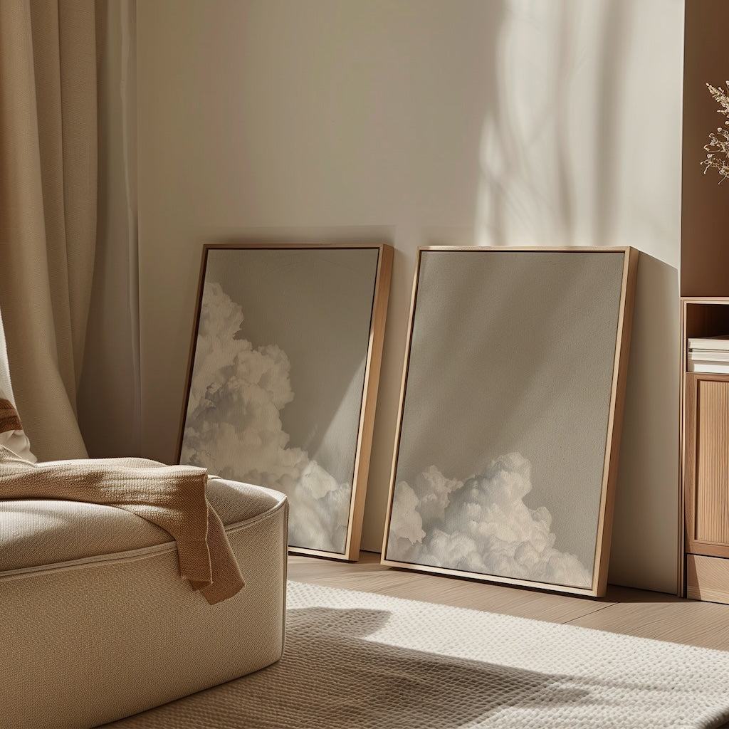The Clouded Dreams Set of 2 framed wall art prints rests against a beige wall in a sunlit, minimalist room. Soft shadows, neutral decor, and a cozy chair create a calm and serene atmosphere for your living space.