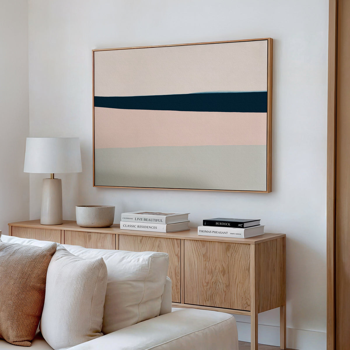 A modern living room corner with a wooden sideboard, white table lamp, stacked books, and a bowl, featuring the Coastal Blend Canvas Art – Horizontal above—perfect for chic living room decor.