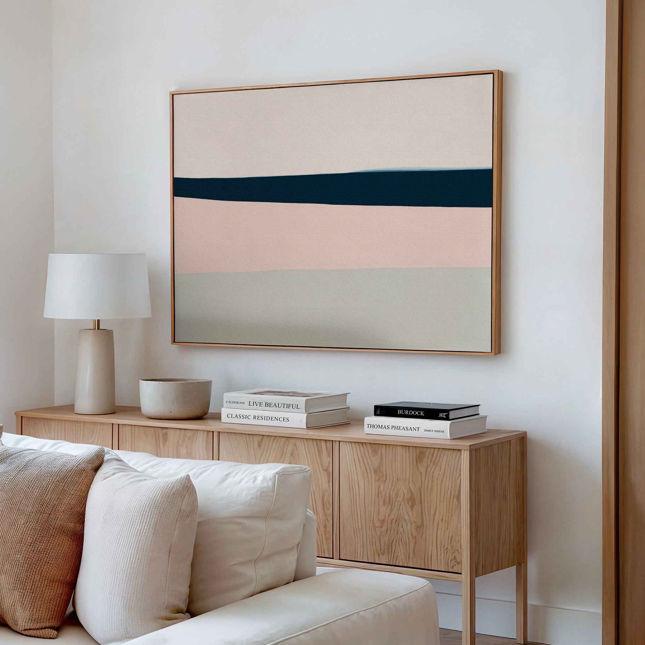 A modern living room corner with a wooden sideboard, white table lamp, stacked books, and a bowl, featuring the Coastal Blend Canvas Art – Horizontal above—perfect for chic living room decor.
