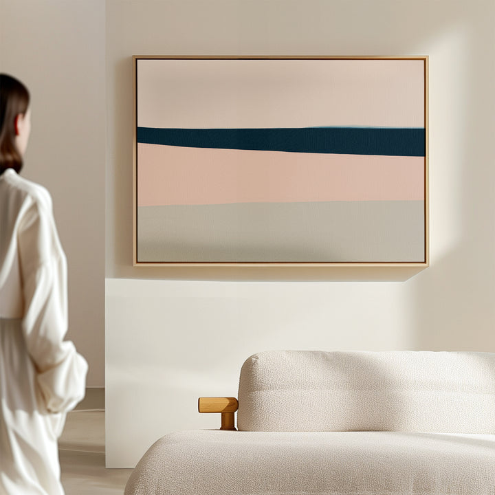 A person in a white shirt admires the Coastal Blend Canvas Art – Horizontal, featuring bands of beige, pink, blue, and gray above a textured cream sofa in a minimal, light-filled room—ideal for modern living room decor.