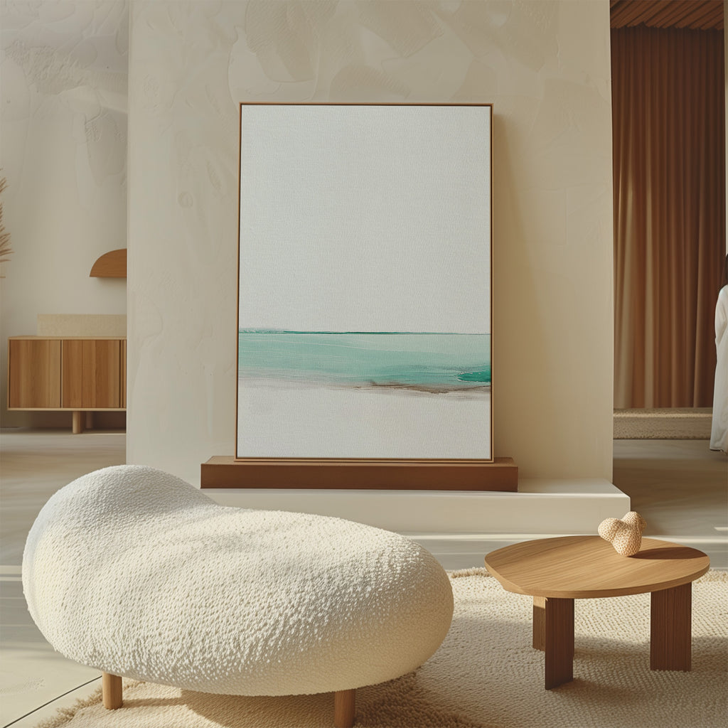 Minimalist living room with a textured white lounge chair, small wooden coffee table with a decorative heart, and the Coastal Breeze Abstract Canvas Art in soft blue and beige tones leaning against the wall.