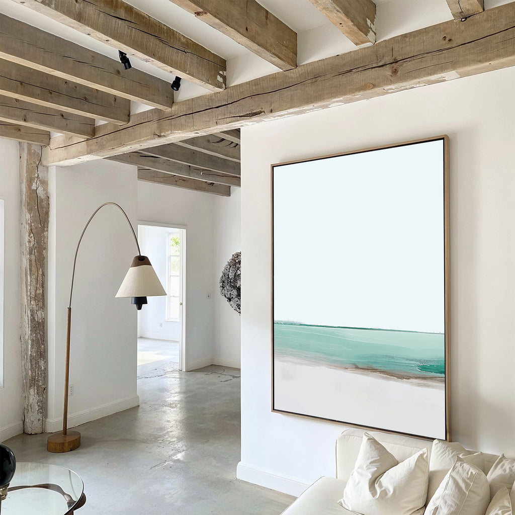 A modern living room with exposed wooden beams, white walls, and a curved floor lamp features the Coastal Breeze Abstract Canvas Art above the sofa, adding a serene touch to the bright, minimalist decor.