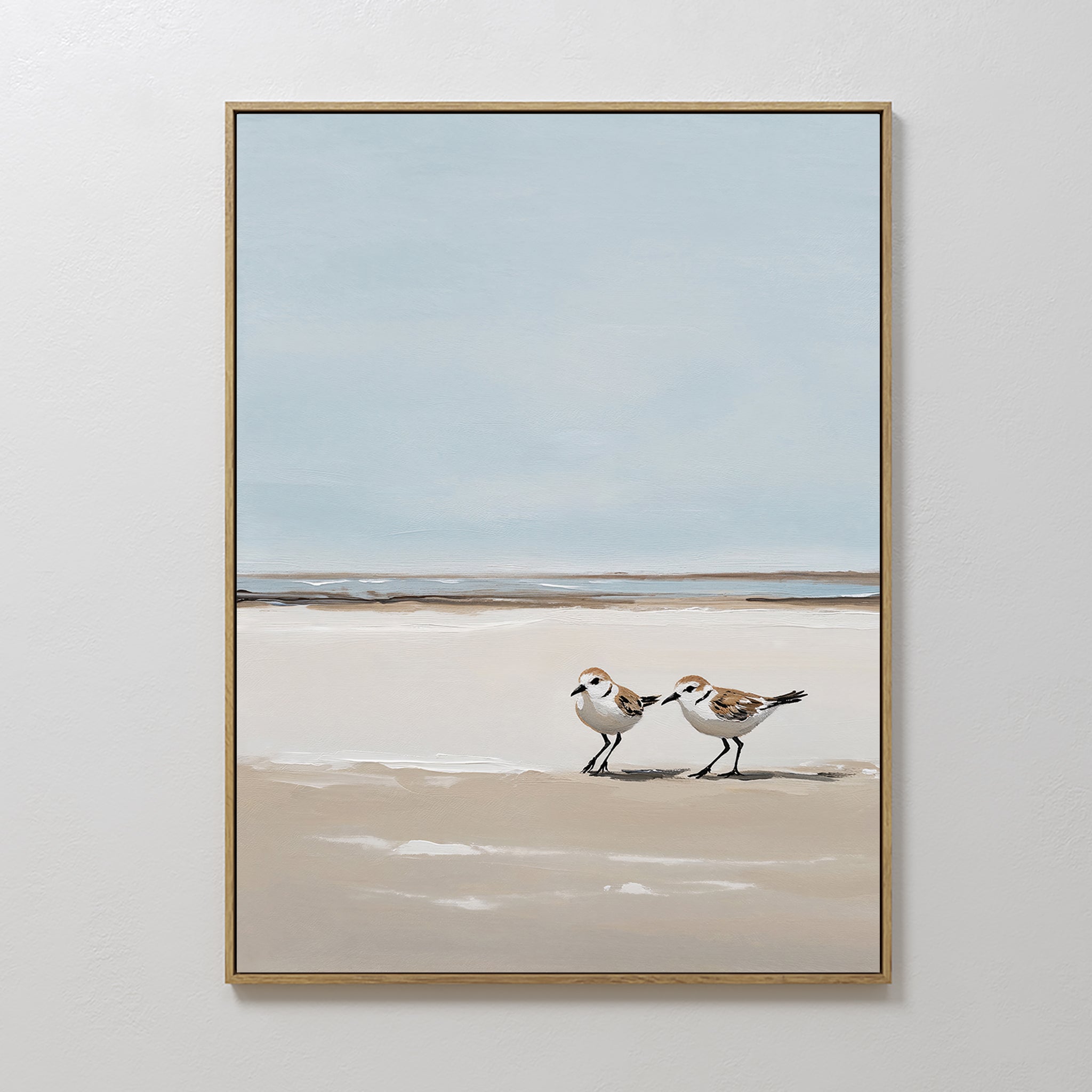 Coastal Chase Canvas Art features two small shorebirds strolling on a sandy beach with gentle waves and a pale blue sky, bringing a calm, minimalist coastal vibe to your space.