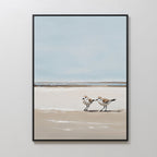 The Coastal Chase Canvas Art features two shorebirds strolling on a sandy beach beneath a calm blue sky with distant water, creating a soft, serene vibe—ideal wall art for tranquil spaces.
