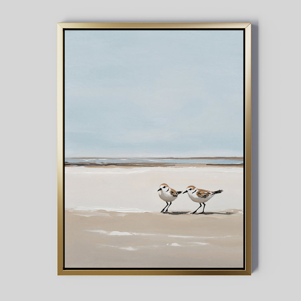 The Coastal Chase Canvas Art features two small shorebirds on a sandy beach with calm waves and a pale blue sky. The gold frame adds an elegant touch to this minimalist, serene wall art print.