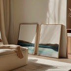 The Coastal Calm Set of 2 features framed abstract landscape paintings in blue and brown tones, resting against a light wall in a sunlit living room, adding modern elegance to your beige-furnished home.