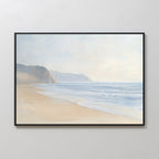 The Coastal Cliffs Canvas Art, featuring gentle waves, sandy shore, and hazy cliffs beneath a cloudy sky, adds serene coastal style to modern home decor when displayed on a plain white wall.