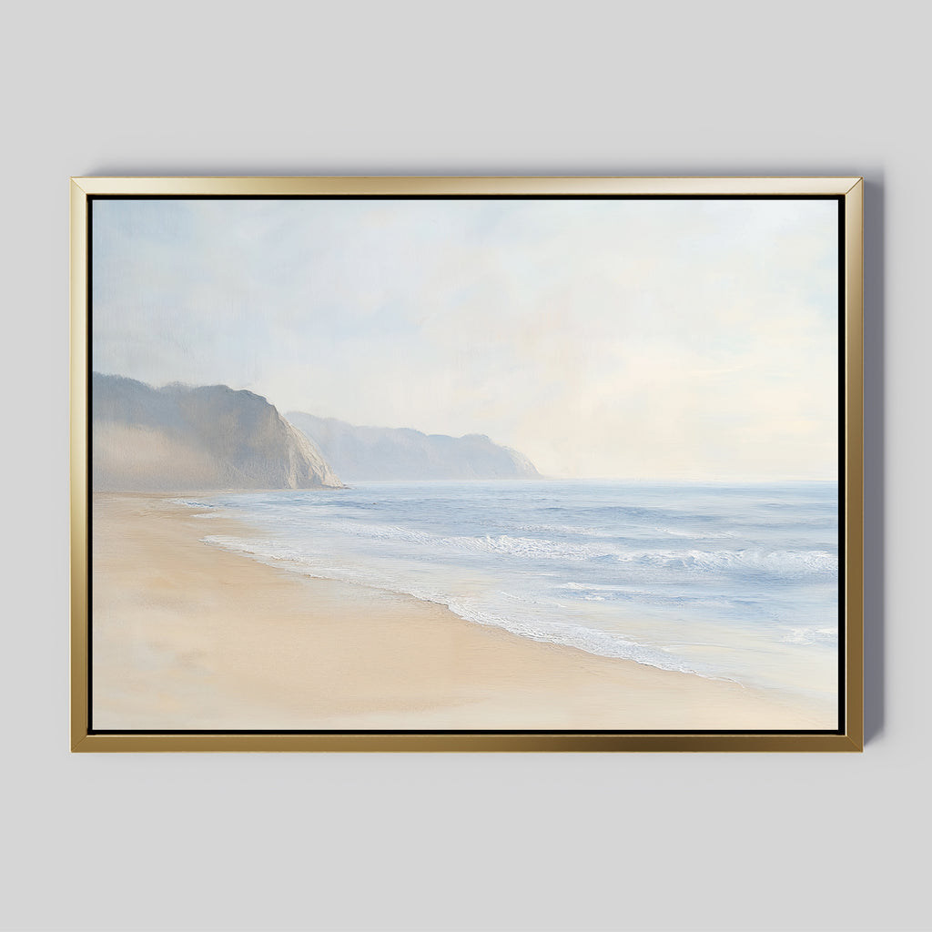 Coastal Cliffs Canvas Art features a serene beach with gentle waves and distant cliffs under a misty sky, framed in gold and black—an ideal tranquil accent for modern decor on pale gray walls.