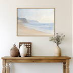 A wooden table with vases and a basket stands by a pale wall, topped with the Coastal Cliffs Canvas Art—a framed print of a serene beach, gentle waves, and distant cliffs—ideal for modern home decor.