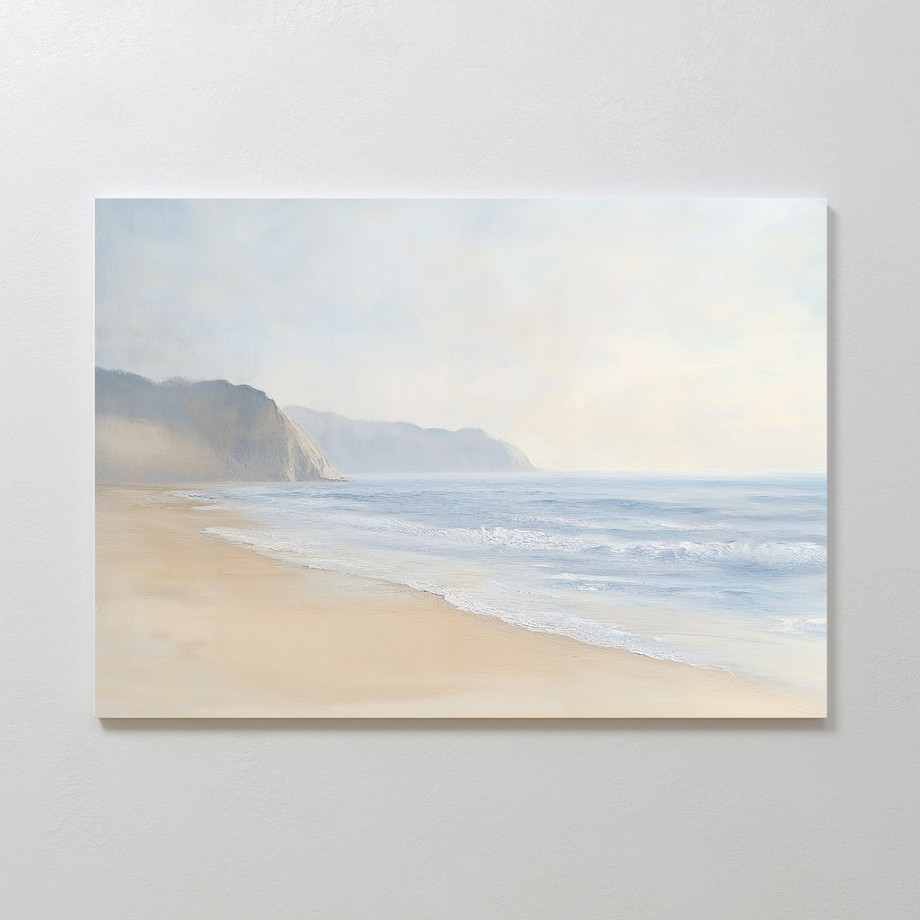 Coastal Cliffs Canvas Art features a serene beach with gentle waves, sandy shore, and distant cliffs under a hazy sky—ideal minimalist wall art for modern home decor, beautifully mounted on a white wall.