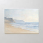 Coastal Cliffs Canvas Art features a serene beach with gentle waves, sandy shore, and distant cliffs under a hazy sky—ideal minimalist wall art for modern home decor, beautifully mounted on a white wall.