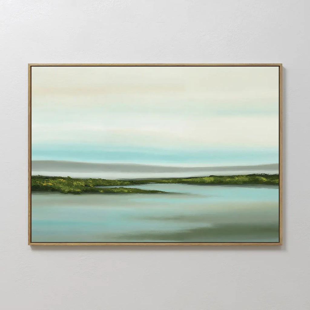 Coastal Marsh Canvas Art is a framed minimalist wall piece showcasing green fields, calm blue water, and a pale layered sky—ideal landscape wall art for bedroom decor on light-colored walls.