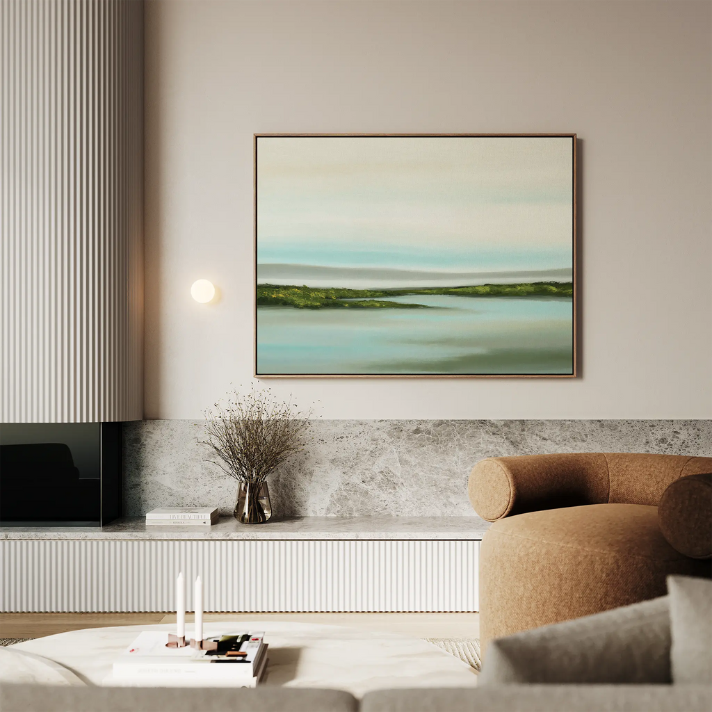 A modern living room with a beige sofa, marble accent wall, and the Coastal Marsh Canvas Art—a green and blue abstract landscape—hanging above a low console. A vase with dried branches sits on the counter.