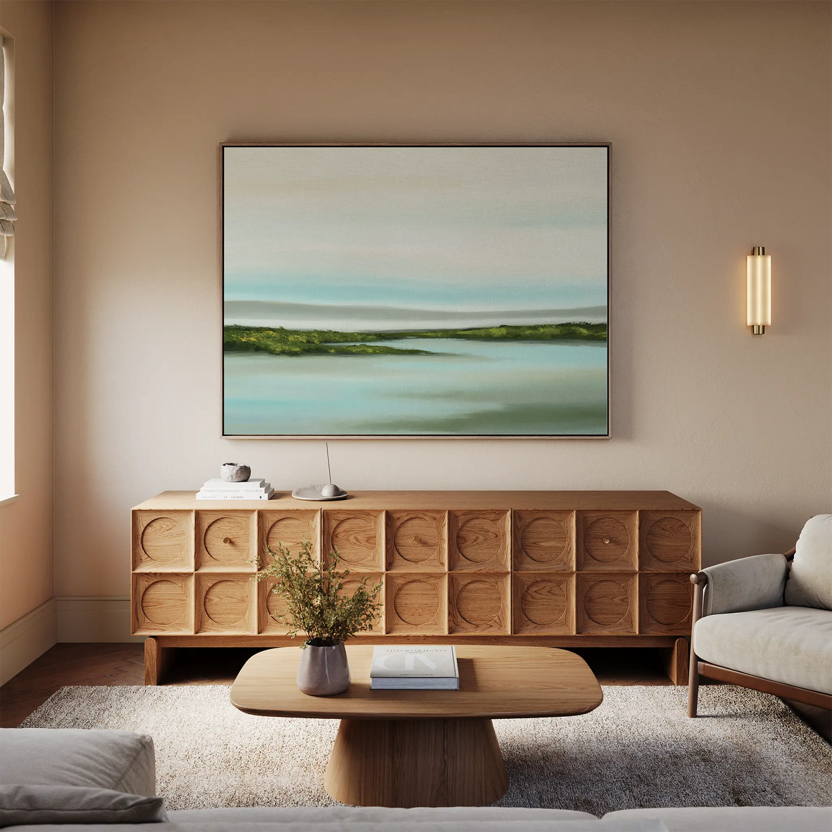 A cozy living room with a wooden sideboard, sofa, and coffee table features minimalist wall art—a large Coastal Marsh Canvas Art in soft blue and green tones above the sideboard. A vase with flowers sits on the coffee table.
