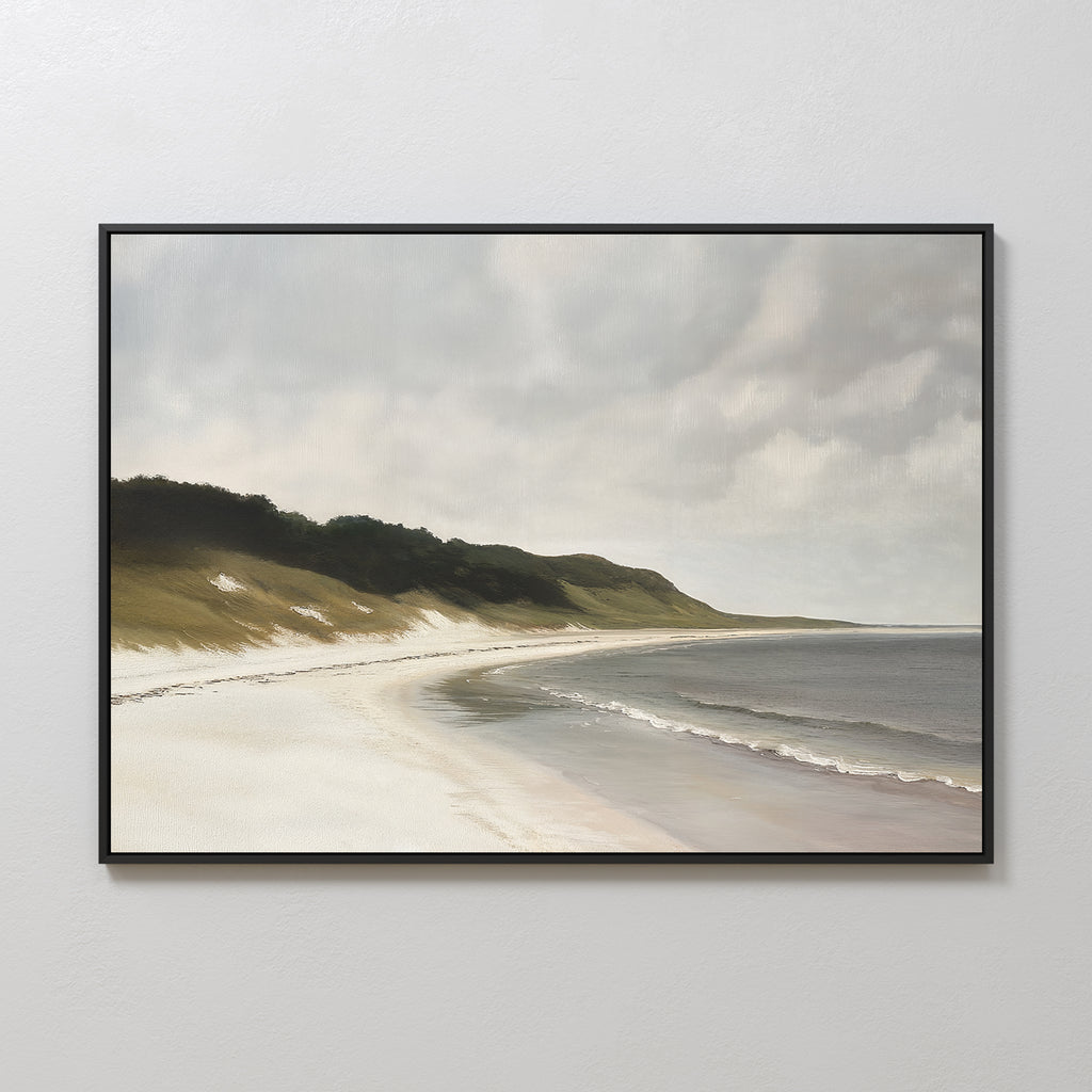The Coastal Silence Canvas Art is a framed wall piece featuring a serene beach landscape with gentle waves, grassy dunes, and a cloudy sky, displayed on a light-colored wall.
