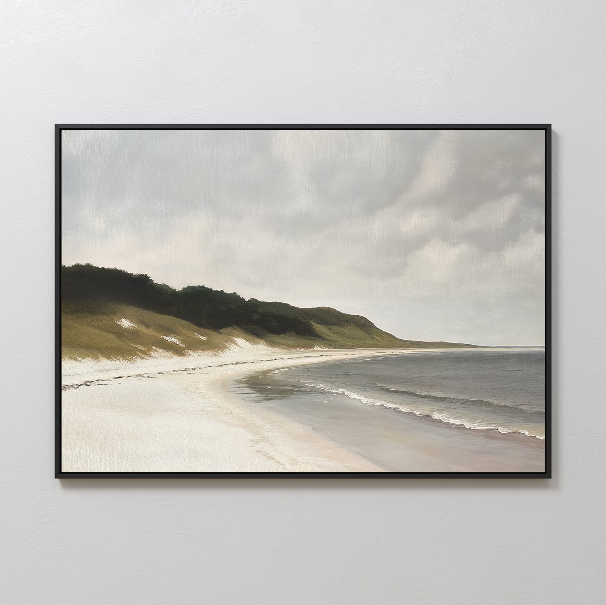 The Coastal Silence Canvas Art is a framed wall piece featuring a serene beach landscape with gentle waves, grassy dunes, and a cloudy sky, displayed on a light-colored wall.