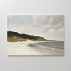 The Coastal Silence Canvas Art showcases a serene sandy beach with gentle waves, grassy dunes, and a cloudy sky, creating calming coastal wall art for your home.