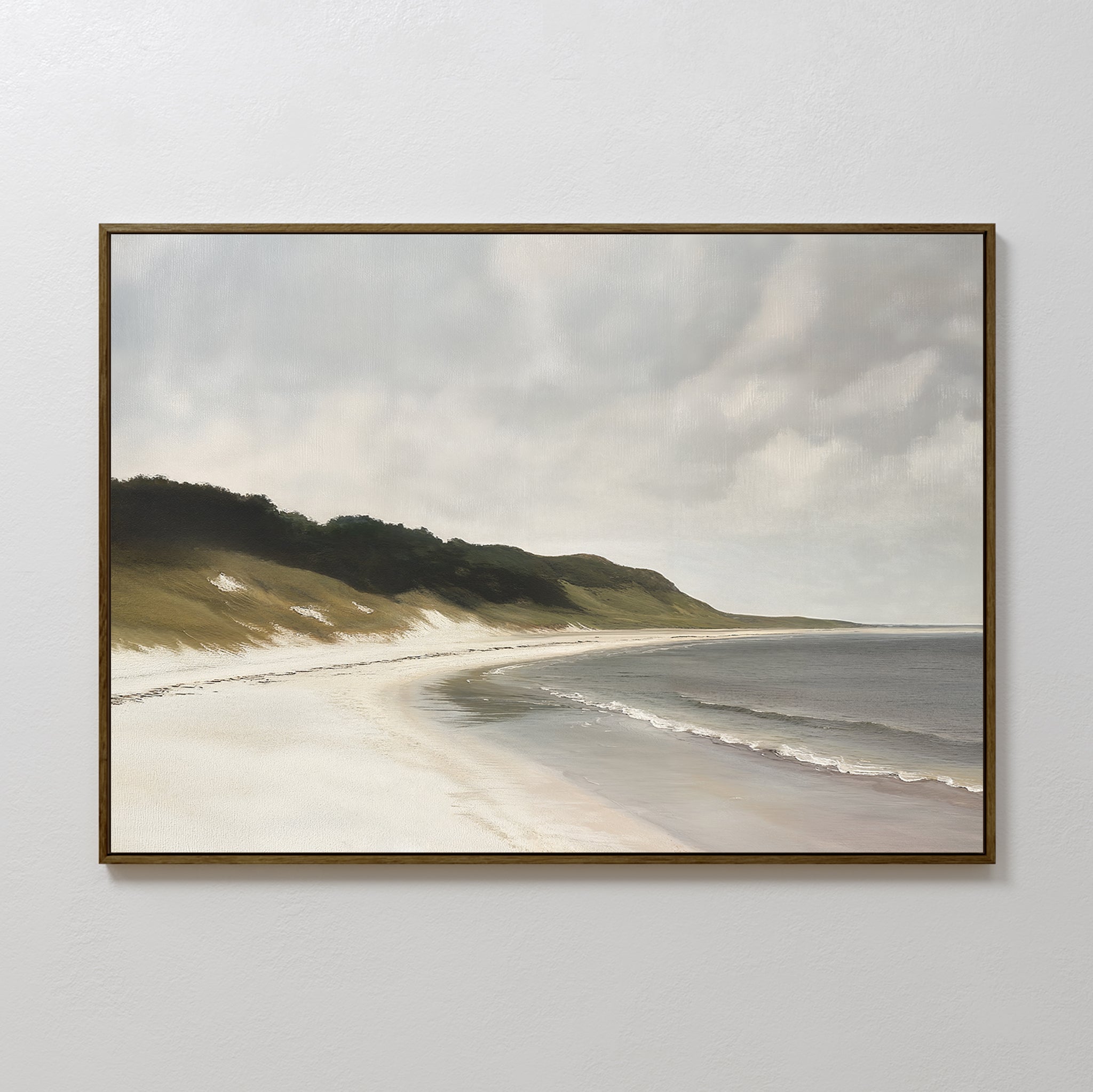 The Coastal Silence Canvas Art, featuring a quiet beach with gentle waves, sandy shore, and grassy dunes beneath a cloudy sky, hangs on a plain white wall.