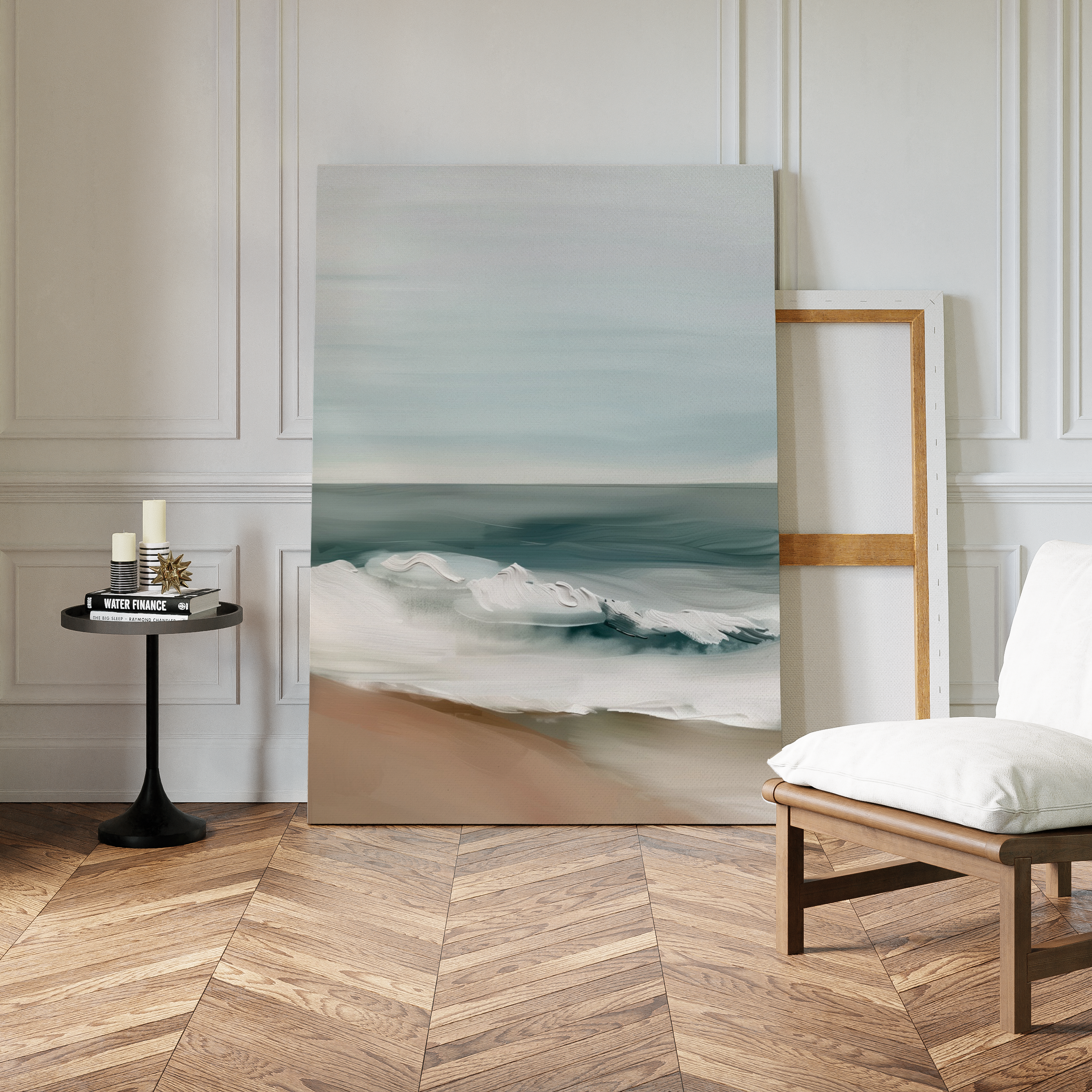 The Coastal Whisper Abstract Canvas Art, perfect as minimalist wall decor, leans against a white paneled wall beside a blank wooden frame. Nearby, a black side table holds candles and books next to a cushioned wooden chair on the herringbone floor.