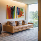 A modern living room with a tan leather sofa, three patterned pillows, the Color Cascade Set of 2 as vibrant abstract wall art, a large window with sheer curtains, and a decorative vase on the floor.