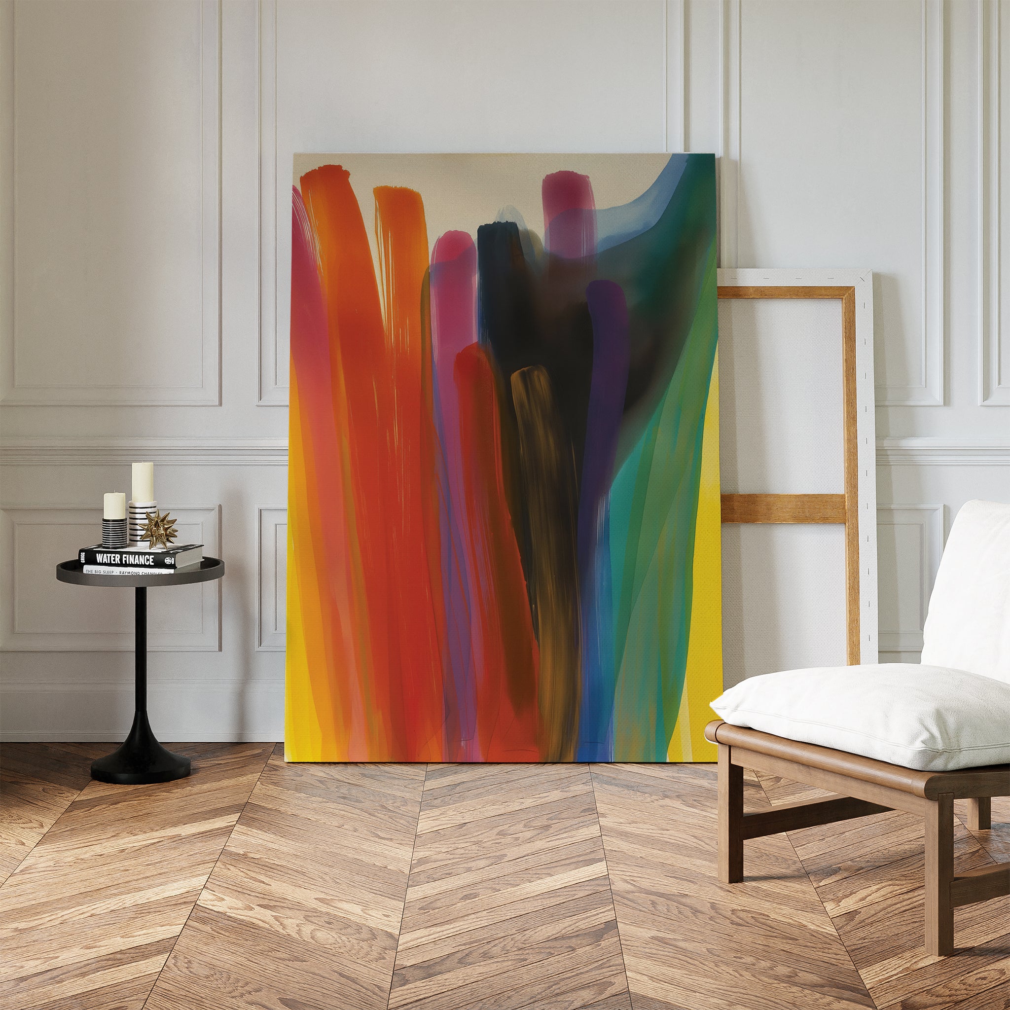 The Color Cascade Abstract Canvas Art, featuring bold vertical brushstrokes, leans against a white wall in a bright room with an empty wooden frame, modern side table with candles, and a cushioned chair on herringbone floors.