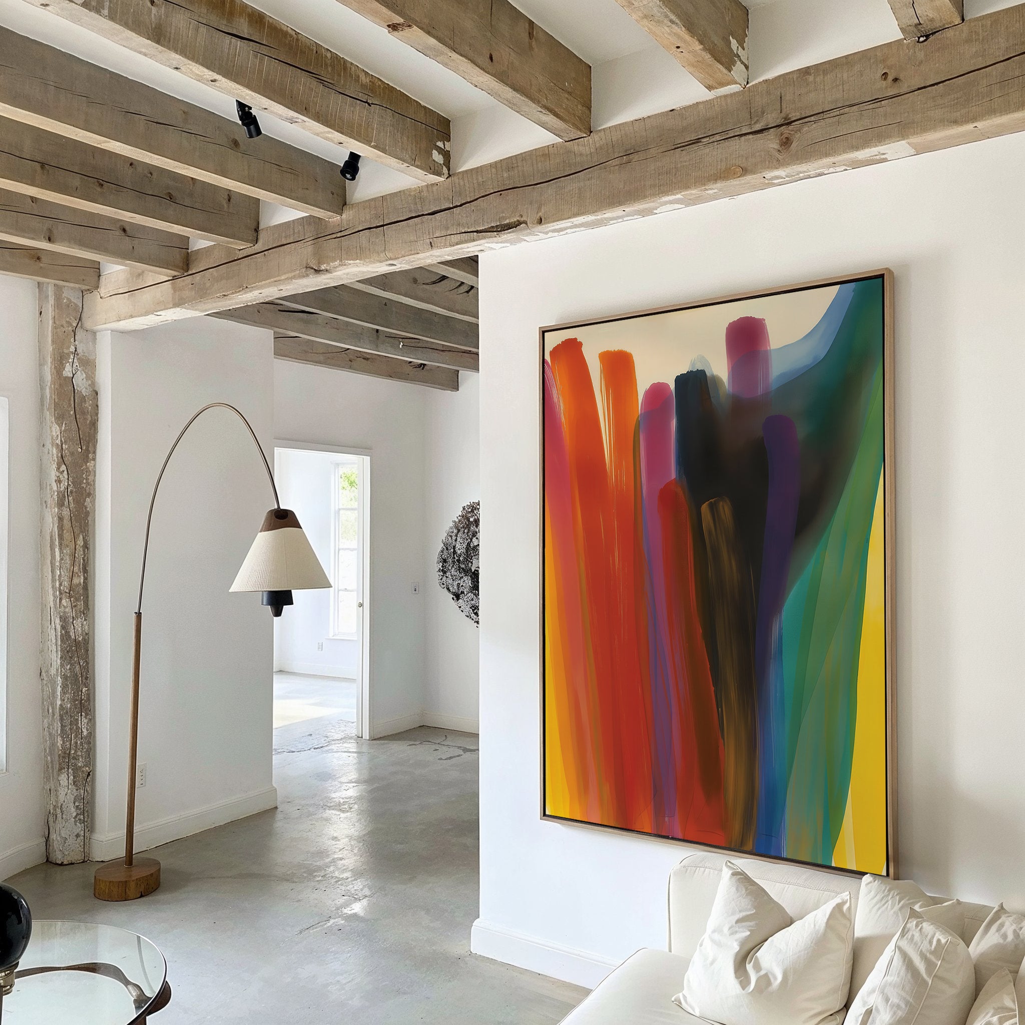A modern living room with exposed wooden beams, white walls, a curved floor lamp, and the Color Cascade Abstract Canvas Art featuring bold red, orange, blue, purple, and yellow swaths. A white sofa is partially visible.
