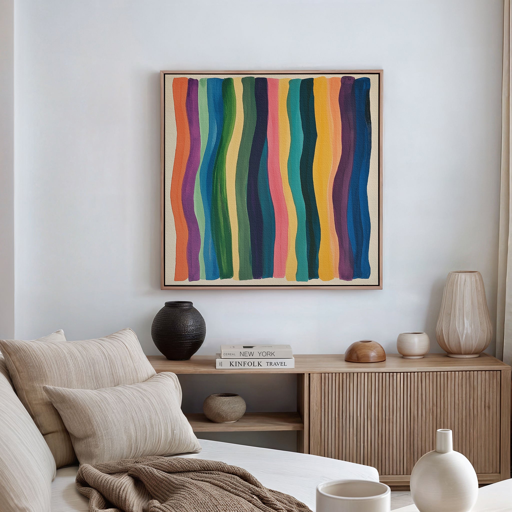 A modern living room with a beige sofa, neutral pillows, a wooden sideboard with decorative vases, and the Color Flow Canvas Art featuring colorful vertical wavy stripes on a white wall.