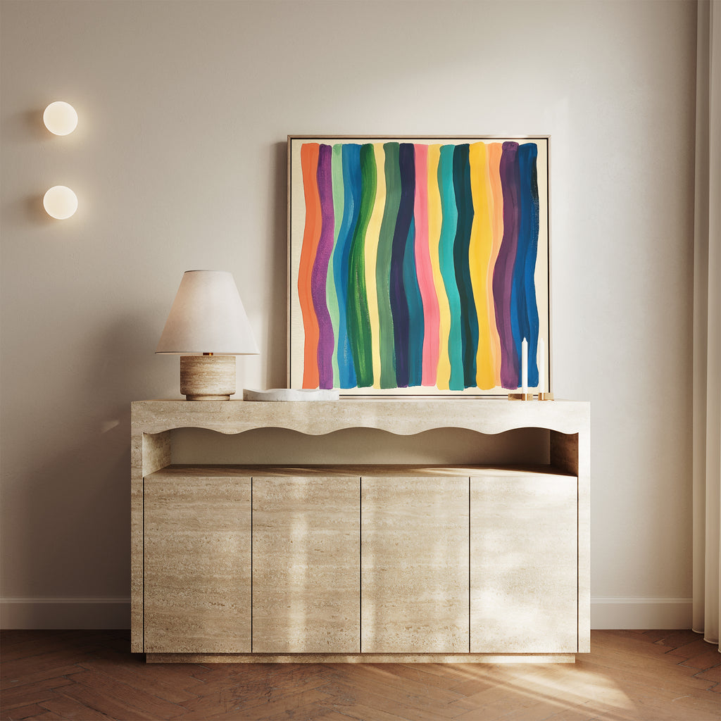 A beige sideboard with a wavy-edged top displays a modern lamp and the Color Flow Canvas Art, which features colorful vertical stripes. Two round wall lights on the neutral wall above complete this stylish living room decor.