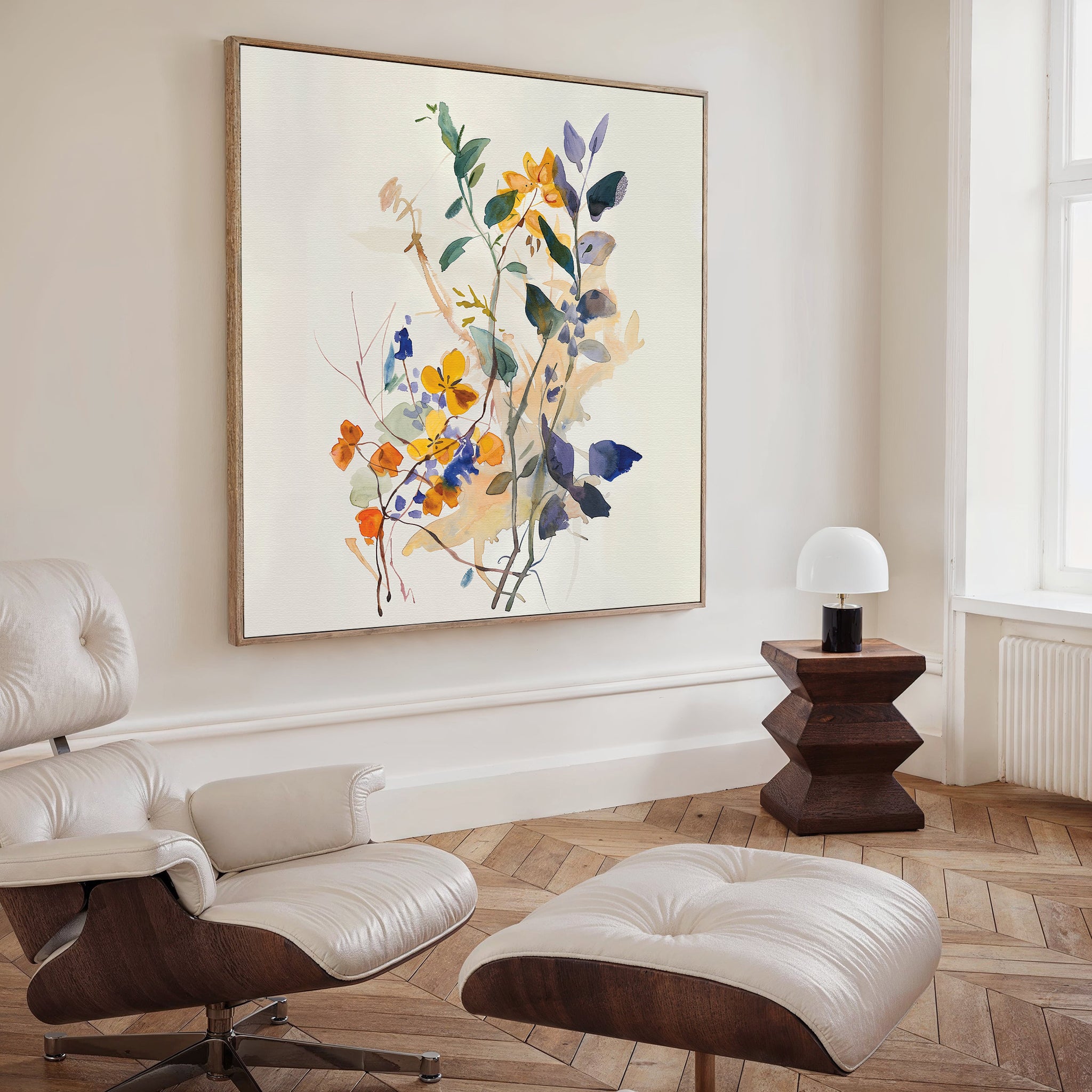 A modern living space features a white leather lounge chair and ottoman, a dark wood side table with a small white lamp, and striking Colorful Branches Canvas Art. Natural light streams in through a tall window.