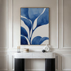 A modern console table with black legs and a white marble top holds candles, a small jar, and a white vase. Above it hangs Cool Tangle Canvas Art—a large abstract botanical painting in blue and white on a light wall.