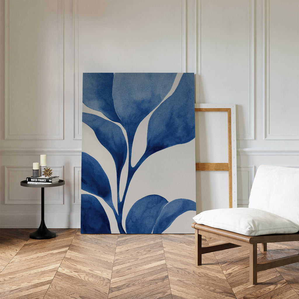 A minimalist room with white paneled walls, a cushioned chair, candles and books on a round black side table, and the Cool Tangle Canvas Art leaning against the wall on a herringbone wood floor.