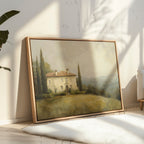 The Country Villa Canvas Art, showcasing a Mediterranean house and cypress trees, leans against a sunlit wall in a bright, minimalist room with soft shadows and light wooden floors.