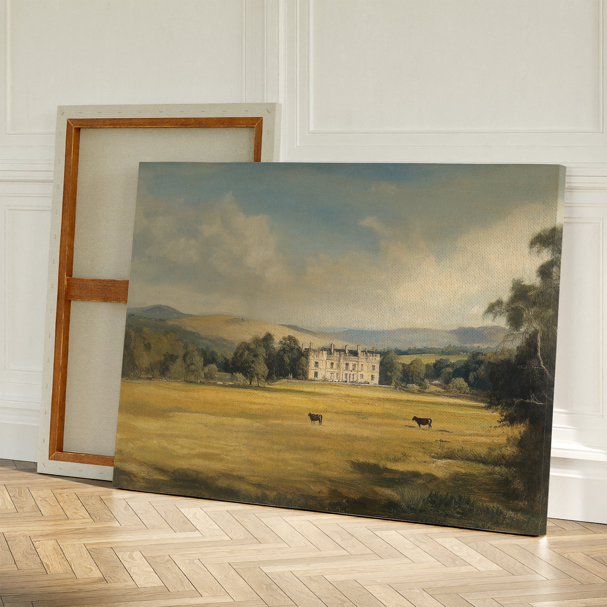 Countryside Dream Canvas Art features a large country house amid trees and grazing cows, leaning beside a blank canvas on a wooden floor—ideal vintage wall art to enhance your countryside decor.