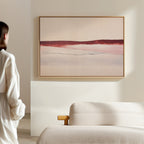 A person in a white shirt stands in a neutral-toned room, admiring the Crimson Horizon Abstract Canvas Art—modern wall decor with soft red, pink, and beige lines above a light sofa, perfect for contemporary living spaces.