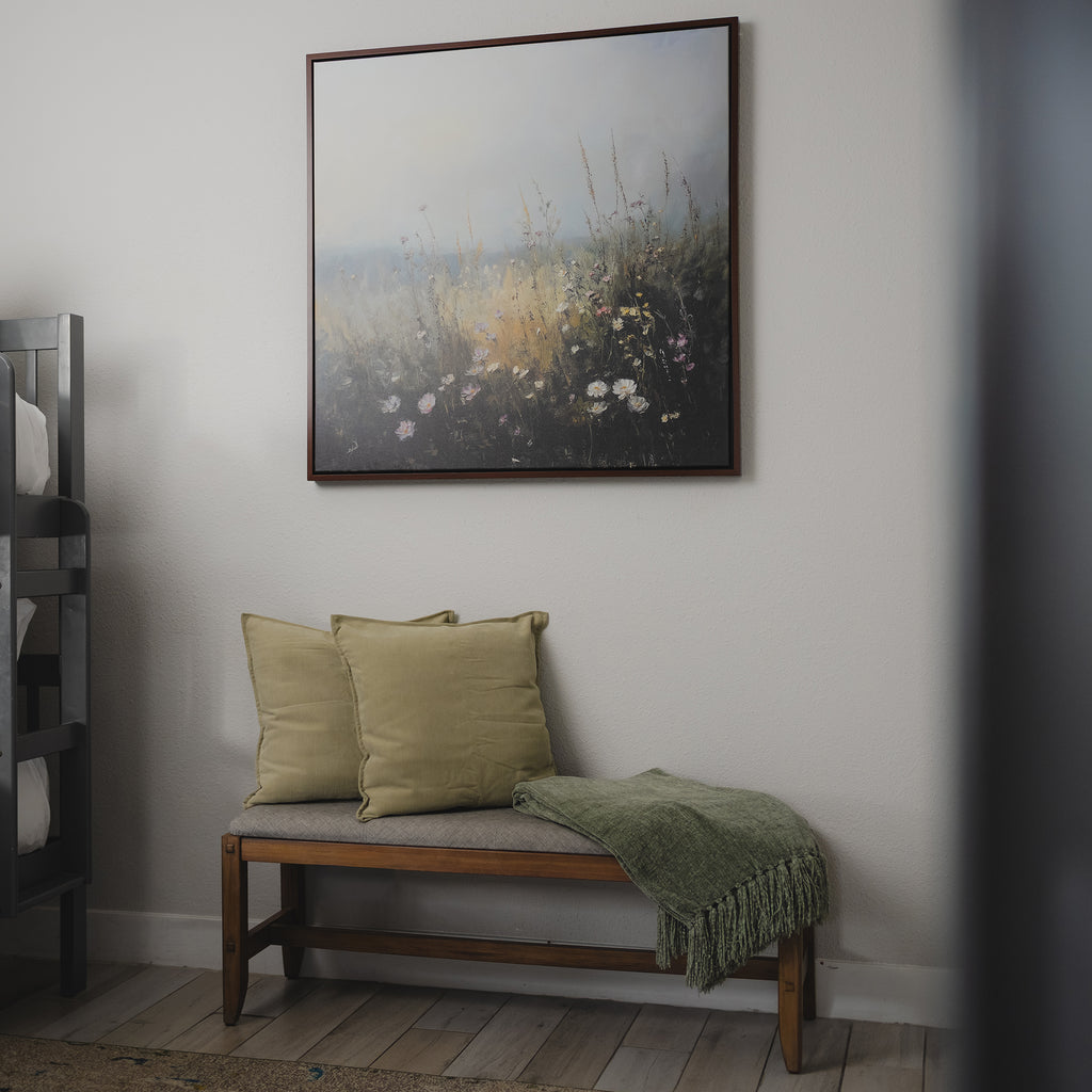 A wooden bench with two light green cushions and a green throw sits beneath the Wildflowers Canvas Art on a white wall, creating a calm, minimalist charm that’s ideal for your living room decor.