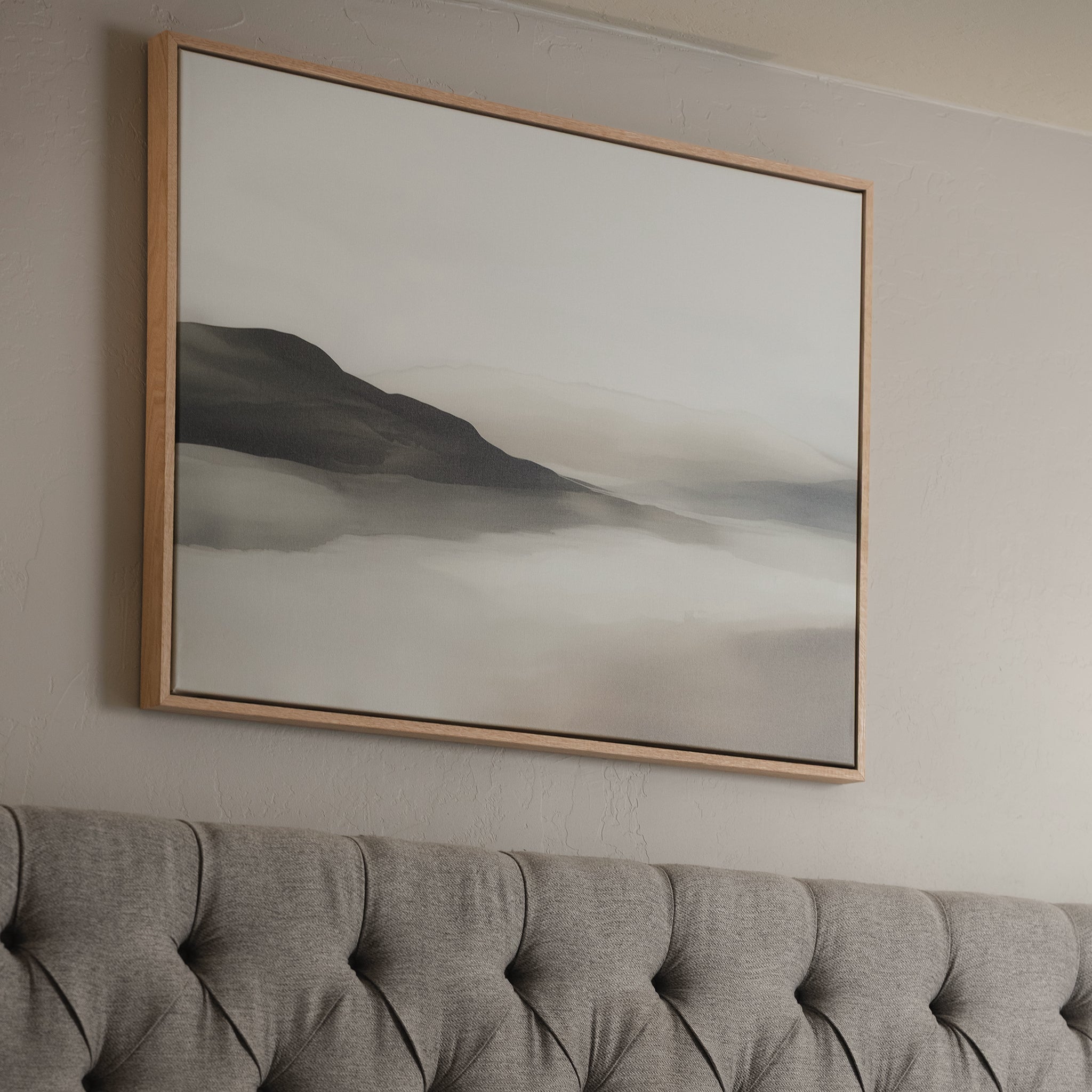 The Soft Valley Canvas Art – Horizontal hangs above a tufted gray headboard, showcasing misty mountains in neutral tones for a calming, minimalist accent that enhances any decor.