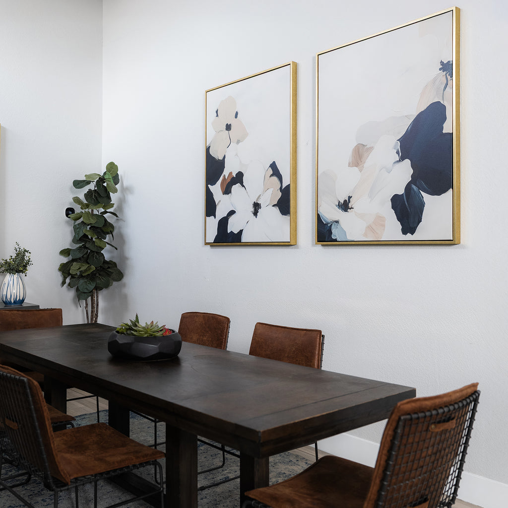 A modern dining room with a dark wooden table, six brown chairs, a potted plant in the corner, the Floral Serenity Set of 2 minimalist wall art on the wall, and a dark centerpiece on the table.