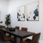 A modern dining room with a dark wooden table, six brown chairs, a potted plant in the corner, the Floral Serenity Set of 2 minimalist wall art on the wall, and a dark centerpiece on the table.